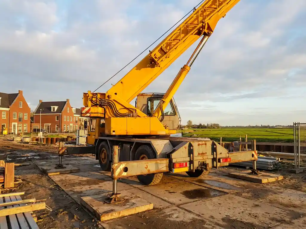 Gele telescoopkraan met uitgeschoven giek op Nederlandse bouwplaats tussen rode bakstenen gebouwen in polderlandschap